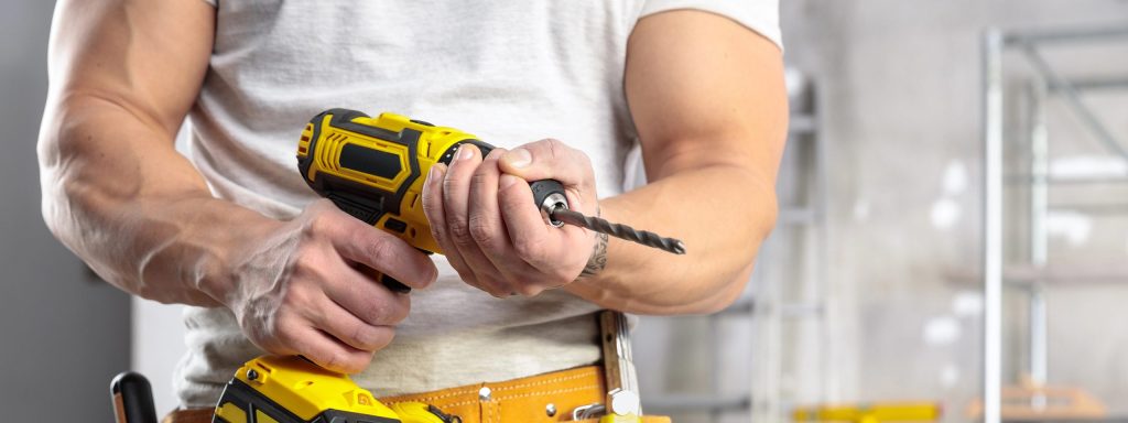 Muscular builder wearing a tool belt holding a battery operated drill in a room under construction in a close up on his hands