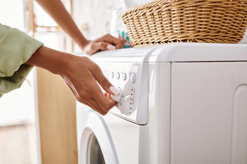 An African American woman loading a dryer onto a washing machine in a bathroom.