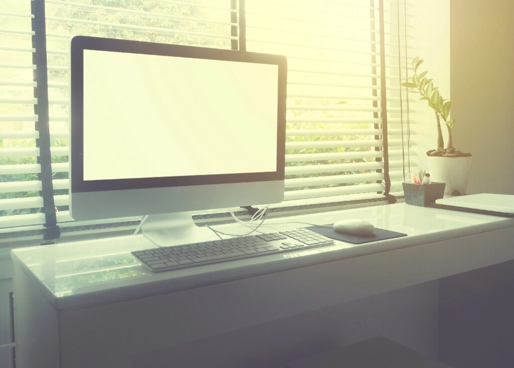 computer on white desk beside window